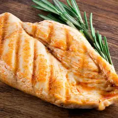 Grillowana pierś kurczaka z rozmarynem na drewnianej desce. Pytanie: ile białka ma kurczak?