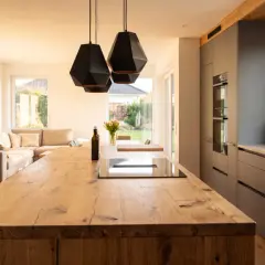 Geräumige Küche mit rustikaler Holzinsel, modernen grauen Schränken und gemütlichem Wohnbereich. Ein schöner industrial landhaus mix.
