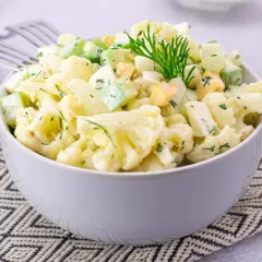 Sałatka z kalafiorem, jajkiem i ogórkiem, udekorowana koperkiem, podana w misce na wzorzystej serwetce.