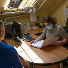Kobieta w maseczce i rękawiczkach pomaga mężczyźnie sprawdzić termin rozprawy sądowej, przeglądając dokumenty.