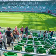 Grupa ludzi wchodzi na zielone trybuny stadionu. W tle widać murawę i napis "WROCŁAW".