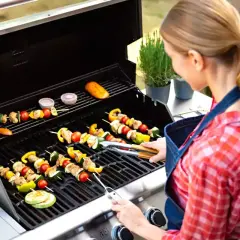 Kvinna grillar spett med kött och grönsaker, som gyros kebab.