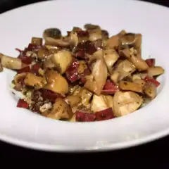 Champiñones al ajillo con jamón, un plato sabroso y aromático, servido en un plato blanco.