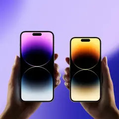 Dwie dłonie trzymają iPhone'y, gdy wyszedł iPhone 15. Jeden z fioletowym gradientem, drugi z żółto-pomarańczowym.