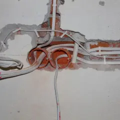 Rozpoczęta wymiana instalacji elektrycznej: widoczne puszki, przewody i fragmenty ceglanej ściany.