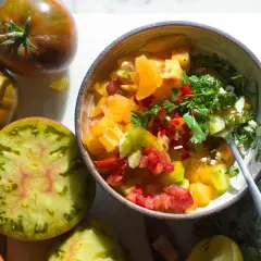 En skål med färgglad pico de gallo, omgiven av olika sorters tomater.