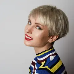 Kobieta z krótkimi blond włosami w stylu pixie, w kolorowym golfie, z czerwonymi ustami.
