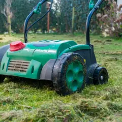 Zielony aerator do trawnika pracuje na wilgotnej trawie, pozostawiając za sobą ślady po wertykulacji.