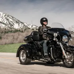 Mężczyzna w kasku i skórzanej kurtce jedzie czarnym motocyklem trójkołowym. W tle góry pokryte śniegiem. Kategoria L5e.