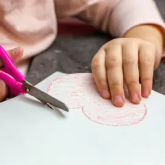 Dziecko uczy się wycinania karty pracy, precyzyjnie tnąc narysowane serce różowymi nożyczkami.