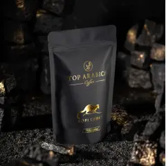 Czarna torebka z napisem "TOP ARABICA Coffee Kopi Luwak" i złotym rysunkiem zwierzęcia. To najdroższa kawa rozpuszczalna, otoczona węglem i złotymi drobinkami.