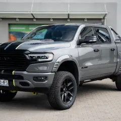 Szary Dodge Ram 1500 z żółtymi akcentami i czarnymi pasami na masce, zaparkowany przed budynkiem.