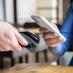 Osoba zbliża telefon do terminala płatniczego, pokazując, jak płacić telefonem.