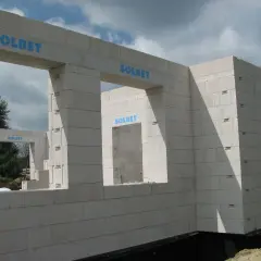 Budowa domu z bloczków SOLBET. Widoczny mur z otworami okiennymi i drzwiami, w tle drzewa i niebo.