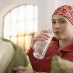 Kobieta w chustce na głowie pije wodę podczas chemioterapii na raka.