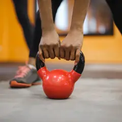 Dłonie zaciskają się na czerwonym kettlebellu. To część treningu fitness, co to za ćwiczenie?