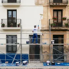 Un pintor en andamios renueva la fachada de un edificio, listo para pintar casa exterior.