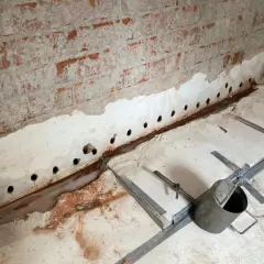 Bohrungen in der Kellerwand deuten auf Maßnahmen gegen aufsteigende Feuchtigkeit hin. Wasser sammelt sich am Boden.
