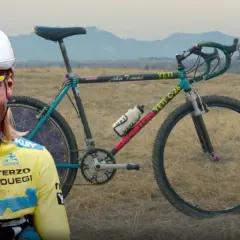 A smiling cyclist in a yellow jersey stands beside a vintage YETI C-26 bike, hinting at where YETI bikes are made.