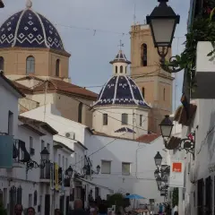 Calle estrecha con casas blancas y cúpulas azules, un ejemplo de los pueblos más bonitos de Alicante.