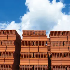 Pile di mattoni forati rossi, pronti per il rinforzo strutturale di muratura portante, sotto un cielo azzurro con nuvole bianche.