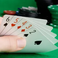 Ręka trzyma karty 6, 5, 4, 3, 2, tworząc strit. W tle stosy żetonów do gry.