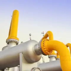 System rur i zbiorników przemysłowych, przez które przepływa gaz ziemny, na tle błękitnego nieba.