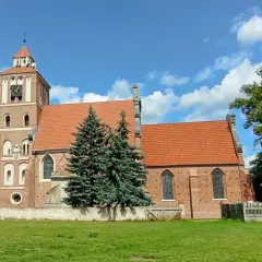 Nieszawa atrakcje: ceglany kościół z wieżą i zegarem, otoczony zielenią, na tle błękitnego nieba z chmurami.