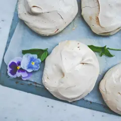 Gotowe bezy na blasze, ozdobione fiołkami i listkami mięty. Idealne do wypróbowania tego przepisu!