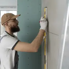 Operaio con livella e matita segna il muro per insonorizzare una stanza dai rumori esterni. Lavori di ristrutturazione in corso.