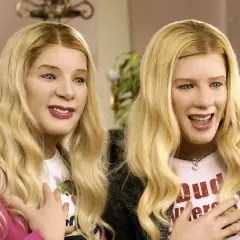 Dwie blondynki w perukach, przypominające bohaterki z filmu "Agenci bardzo specjalni obsada", śmieją się z rękami na piersi.