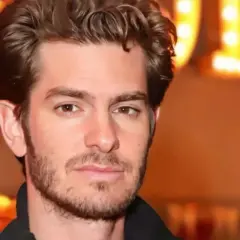 Andrew Garfield, avec une barbe naissante, pose devant des lumières chaudes. On spécule sur son prochain film.