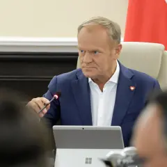 Donald Tusk w Płocku podczas spotkania. Siedzi przy stole z mikrofonem i laptopem.