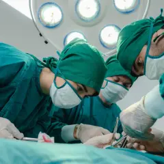 Zespół chirurgów w zielonych fartuchach i maseczkach przeprowadza operację zastawki serca. Skupienie na twarzach, precyzja ruchów.