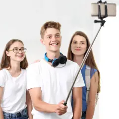 Trzech przyjaciół robi sobie selfie z kijkiem. Chłopak z przodu uśmiecha się szeroko, dziewczyna w okularach po lewej też, a ta z tyłu patrzy w obiektyw. To prosty sposób, jak zrobić ładne zdjęcie grupowe.