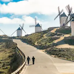 Molinos de viento en la ruta de Don Quijote, con dos personas caminando por un camino.
