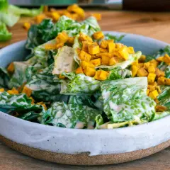 En skål med krispig romansallad, rikligt täckt med krämig caesarsallad dressing och toppad med gyllene krutonger.