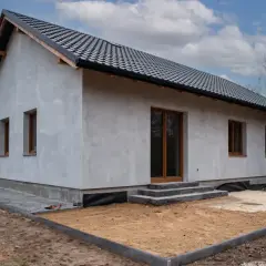 Dom w budowie z szarym tynkiem i brązowymi oknami. Zastanawiasz się, czy drzwi zewnętrzne można odliczyć od podatku?