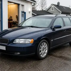 Mörkblå Volvo V70 2.0 Flexifuel står parkerad utanför en verkstad. Kanske är det ett problem med bilen som behöver åtgärdas.