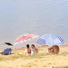 Paraolsole chronią przed słońcem na piaszczystym brzegu, a w tle spokojne **świerklaniec jezioro**.