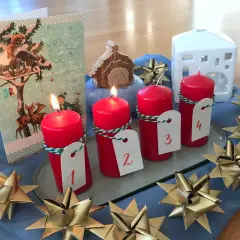 Vier rote Kerzen mit Zahlen 1-4, ein Adventskalender, ein Krippenspiel und goldene Sterne schmücken den Tisch. Perfekt für die Vorfreude auf Weihnachten in der **Advent Grundschule**.