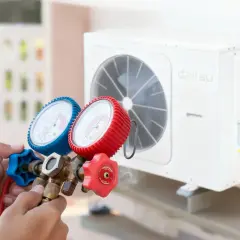 Manos sostienen manómetros conectados a un aire acondicionado Daitsu. Los aires acondicionados vienen con gas, esencial para su funcionamiento.