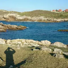 La **playa de Canallave** se asoma entre rocas y aguas turquesas. En la colina, casas de tejados rojos vigilan el mar.