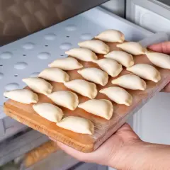 Ręce wkładają deskę z surowymi pierogami do zamrażarki. To prosty sposób, jak przechować ciasto na pierogi na później.