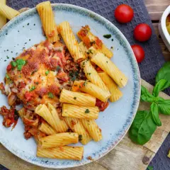 Herzhafter nudelauflauf mit hackfleisch, überbacken mit Käse, serviert mit Rigatoni und frischen Tomaten.