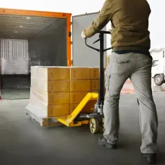 Pracownik magazynu przemieszcza paletę z paczkami za pomocą wózka widłowego, przygotowując towar do **cross trade** transportu.