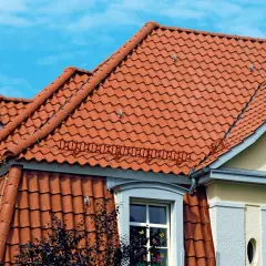 Dwa rodzaje dachów z czerwonej dachówki ceramicznej, jeden płaski, drugi skośny, pod błękitnym niebem.