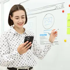 Kobieta z telefonem i markerem przy tablicy z projektami stron. Wyjaśnia, że tekst wyjustowany co to znaczy, pokazując przykłady.