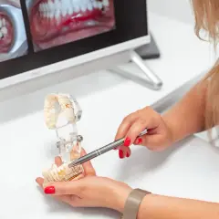 Dentystka omawia na modelu, ile trwa założenie korony na zęba. Na ekranie widać zdjęcia uzębienia.