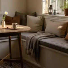 Gemütliche Ecke mit Kissen und Decke, inspiriert vom Gedanken, eine **Eckbank selber bauen** zu wollen. Ein runder Tisch mit Tassen und einer Blume.